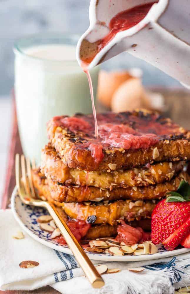 Almond French Toast with Roasted Strawberry Syrup being poured on. There is a glass of milk in the background. 