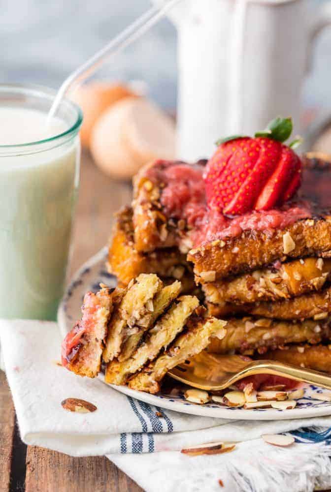 Almond French Toast with Roasted Strawberry Syrup on a fork and a glass of milk in the background. 