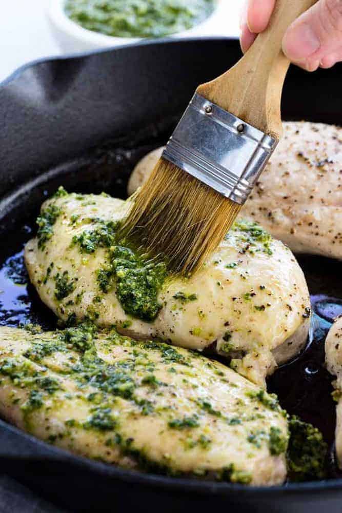 Brushing pesto sauce on chicken breasts.