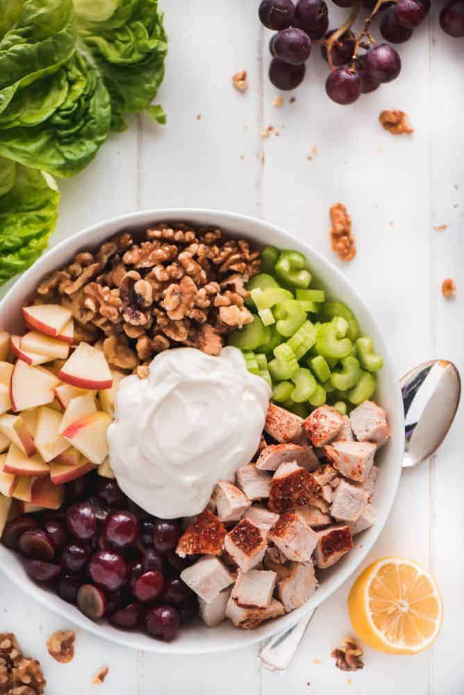 A bowl full of Waldorf Chicken Salad ingredients- Chicken, grapes, apples, walnuts, celery, and dressing.