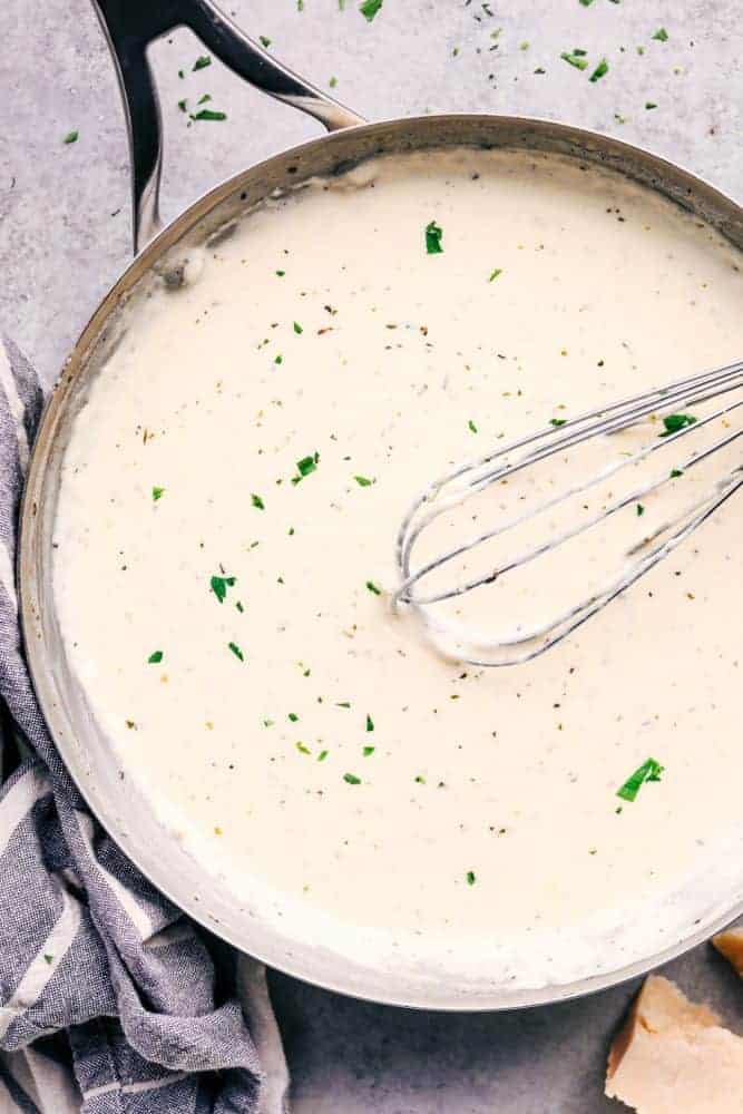 Alfredo sauce in a pan with a whisk. 