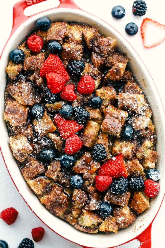 Baked French toast in a pan with fresh blueberries, strawberries and blackberries over top.