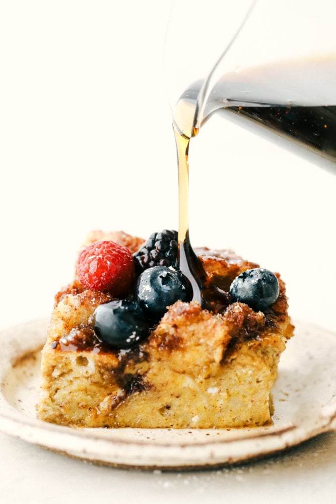 Baked French toast slice on a plate with syrup being poured overtop. 