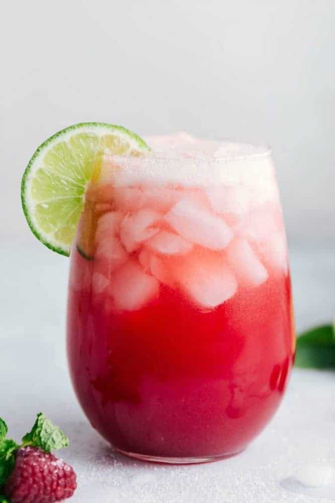 Raspberry Limeade in a clear glass with ice and a sliced lime. 