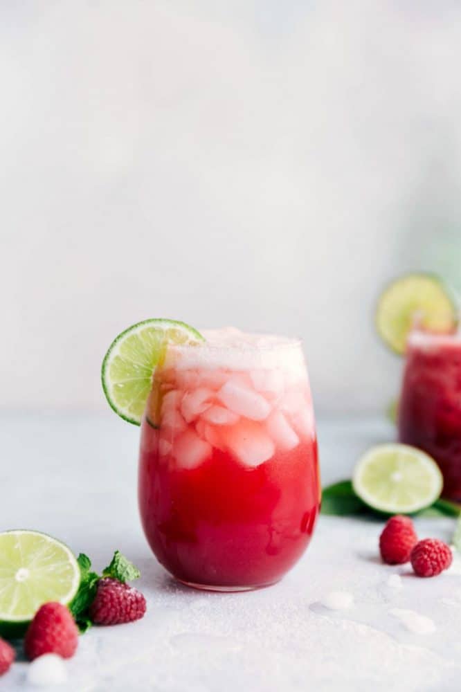 Raspberry Limeade in a clear glass with a sliced lime and fresh raspberries on the table. 