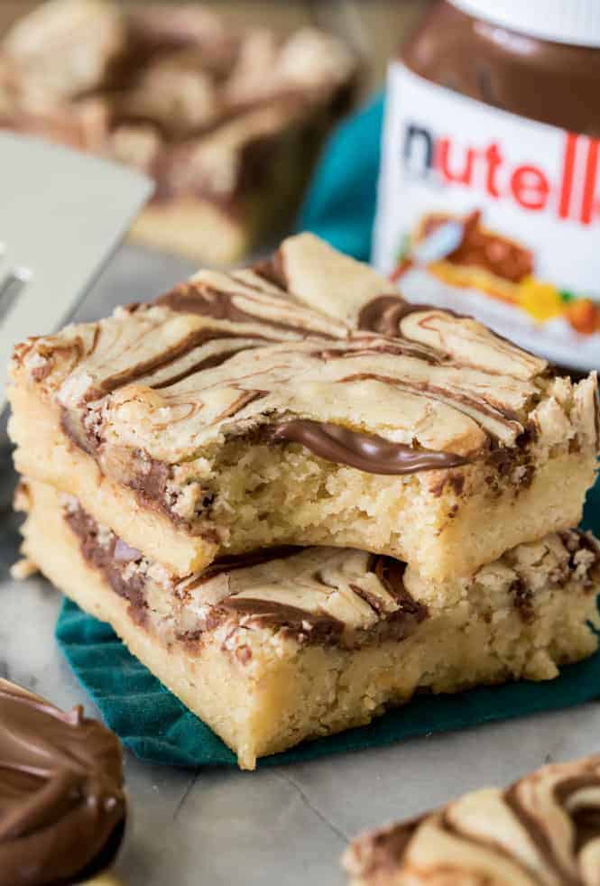 Nutella Blondies stacked on top of one another with a jar of Nutella in background. 