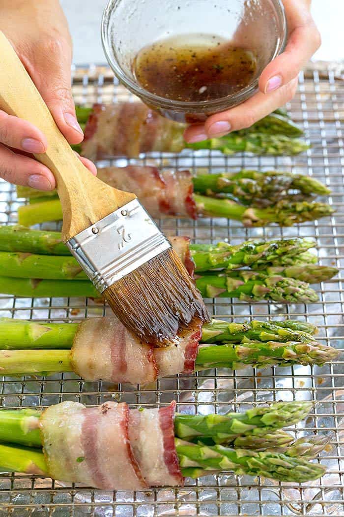 Brushing an olive oil and maple glaze over bacon wrapped asparagus