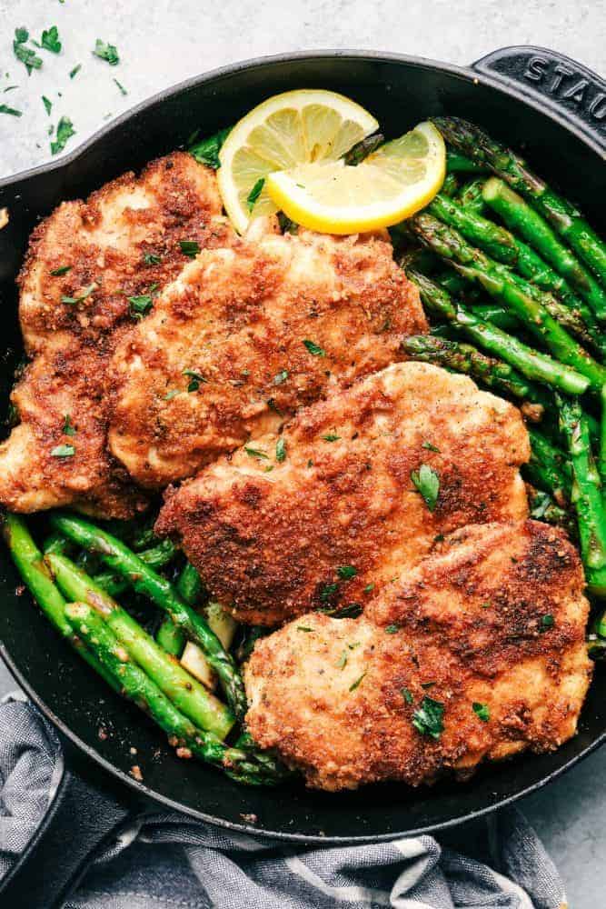 Crispy Garlic Chicken with Asparagus in a skillet with sliced lemon. 