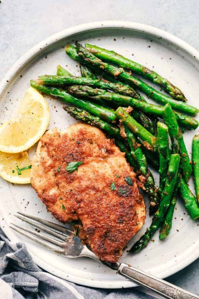 One piece of crispy garlic chicken with asparagus and sliced lemon on a white plate. 