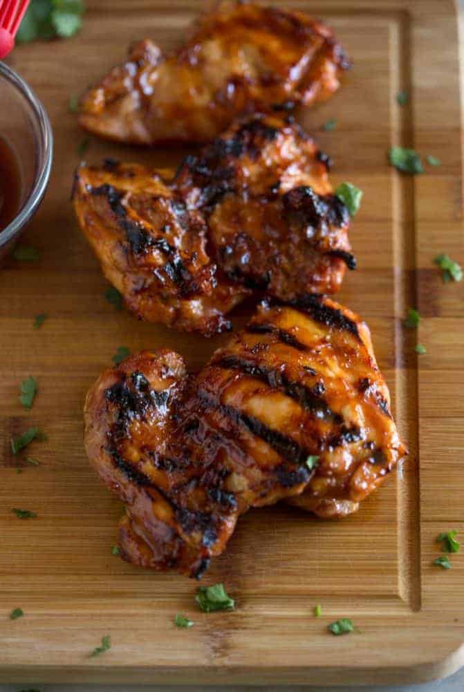 Grilled BBQ chicken thighs resting on a wood cutting board.