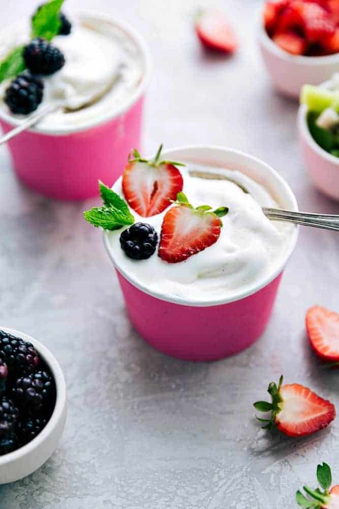 Zwei rosa Pappbecher mit Vanille-Softeis servieren gefrorenen Joghurt.  Auf einem davon sind frische Erdbeeren und auf dem anderen Brombeeren. 