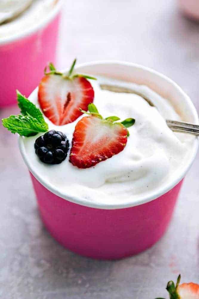 Vanille-Soft-Servier-Frozen-Joghurt in einem rosafarbenen Papierschnitt mit zwei Erdbeeren und einer Brombeere darauf mit einem Metalllöffel. 