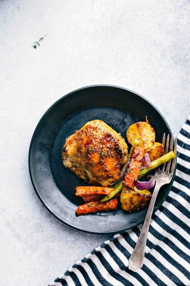 Honey mustard chicken and root vegetables on a black plate with a white fork. 