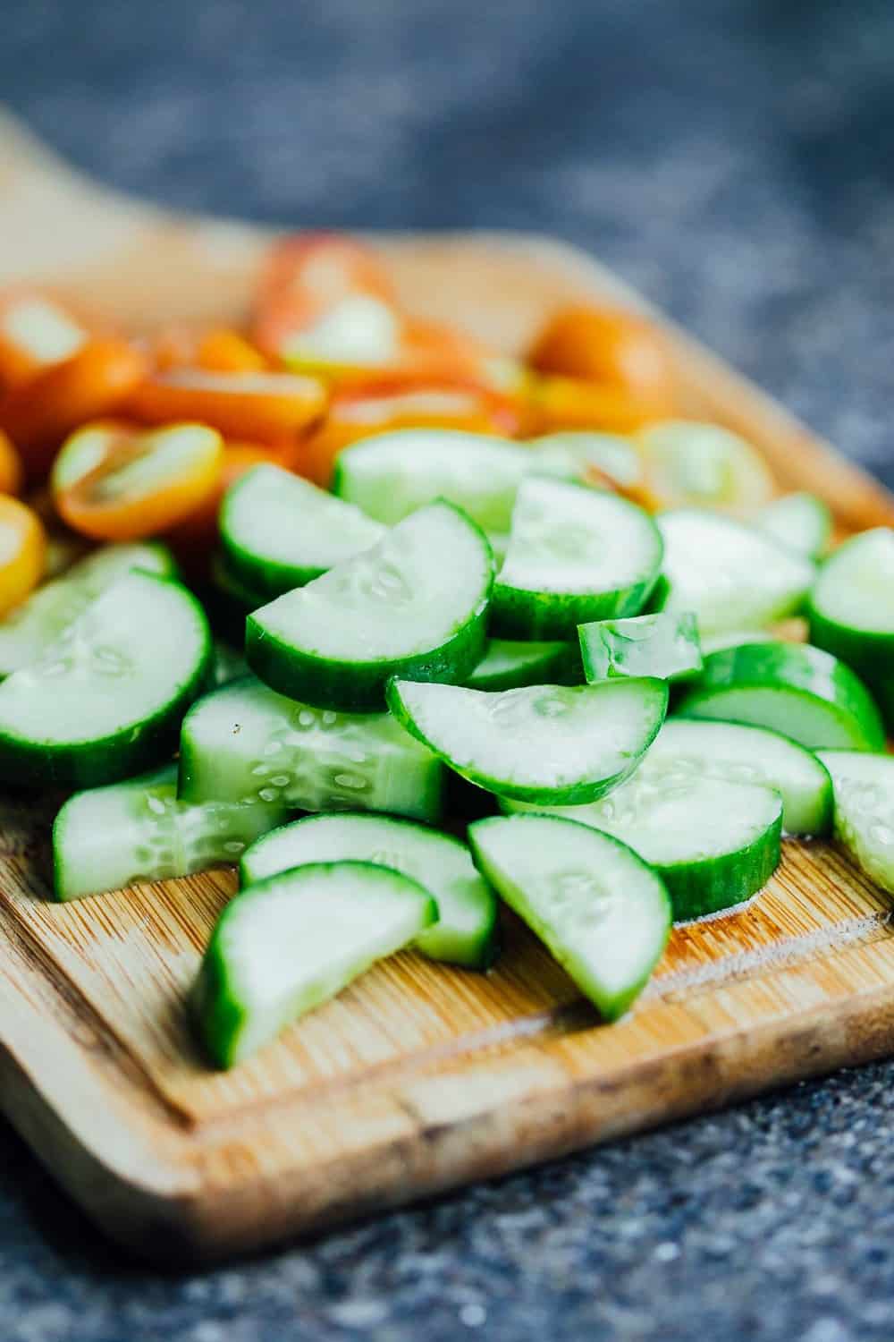 Sliced cucumbers and tomatoes on a cutting board for chilled cucumber tomato salad