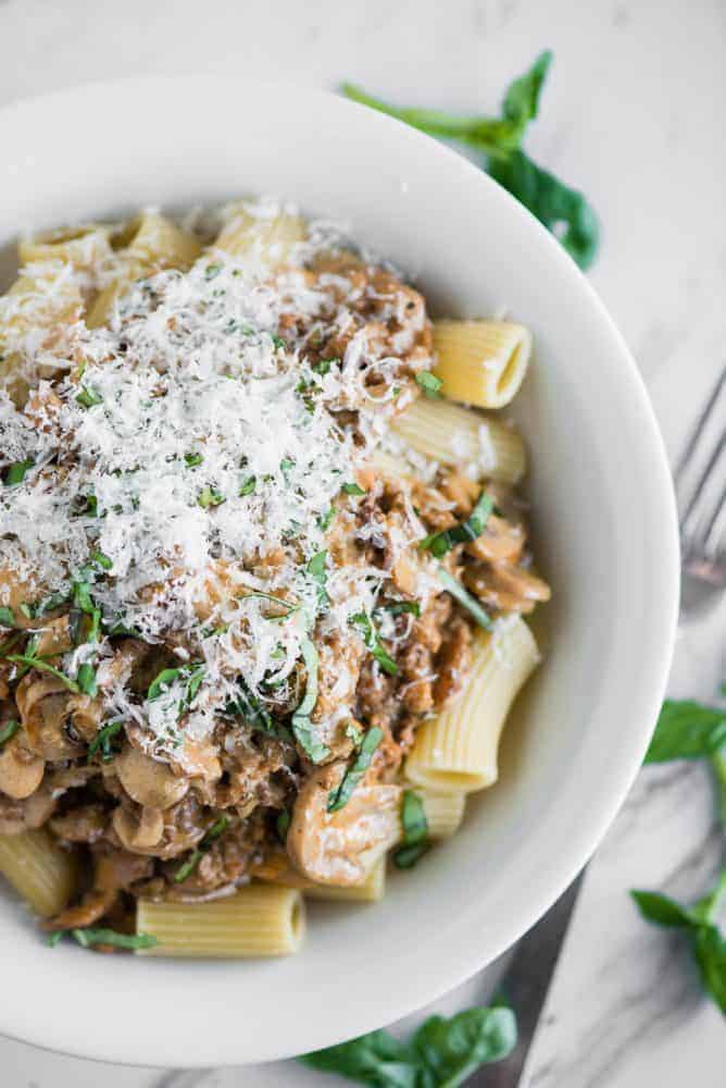 Creamy Sausage Mushroom Rigatoni in a white bowl with a metal fork and garnish on the side. 