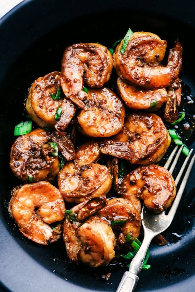 Cajun Garlic Butter Shrimp in a black bowl with a metal fork. 