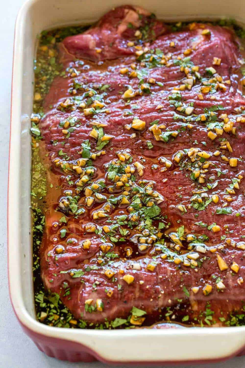 Flank steak marinating in a casserole dish