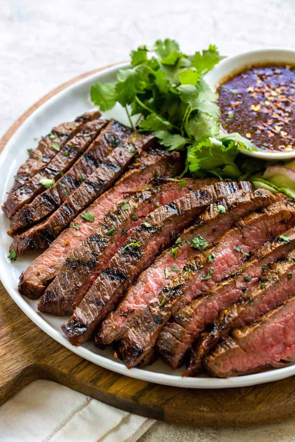 strips of grilled flank steak on a plate served with sauce