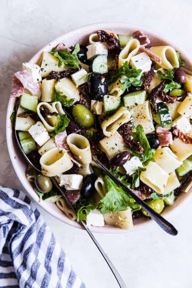 Mediterranean pasta salad in a white bowl with a metal spoon. 