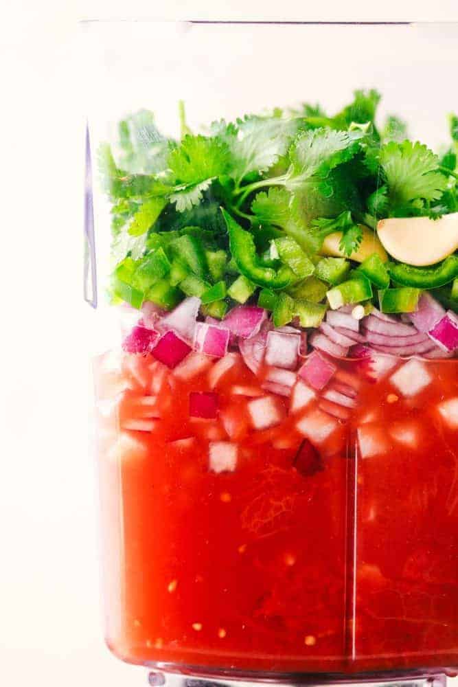 Un-mixed ingredients for blender salsa in a clear blender.