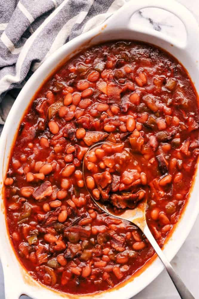Baked Beans in a white platter with a metal spoon. 