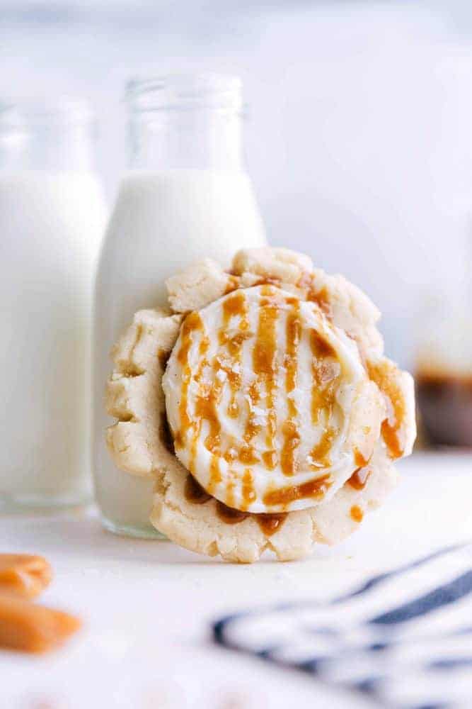 Sugar cookie with cream cheese frosting leaning up against a glass of milk. 