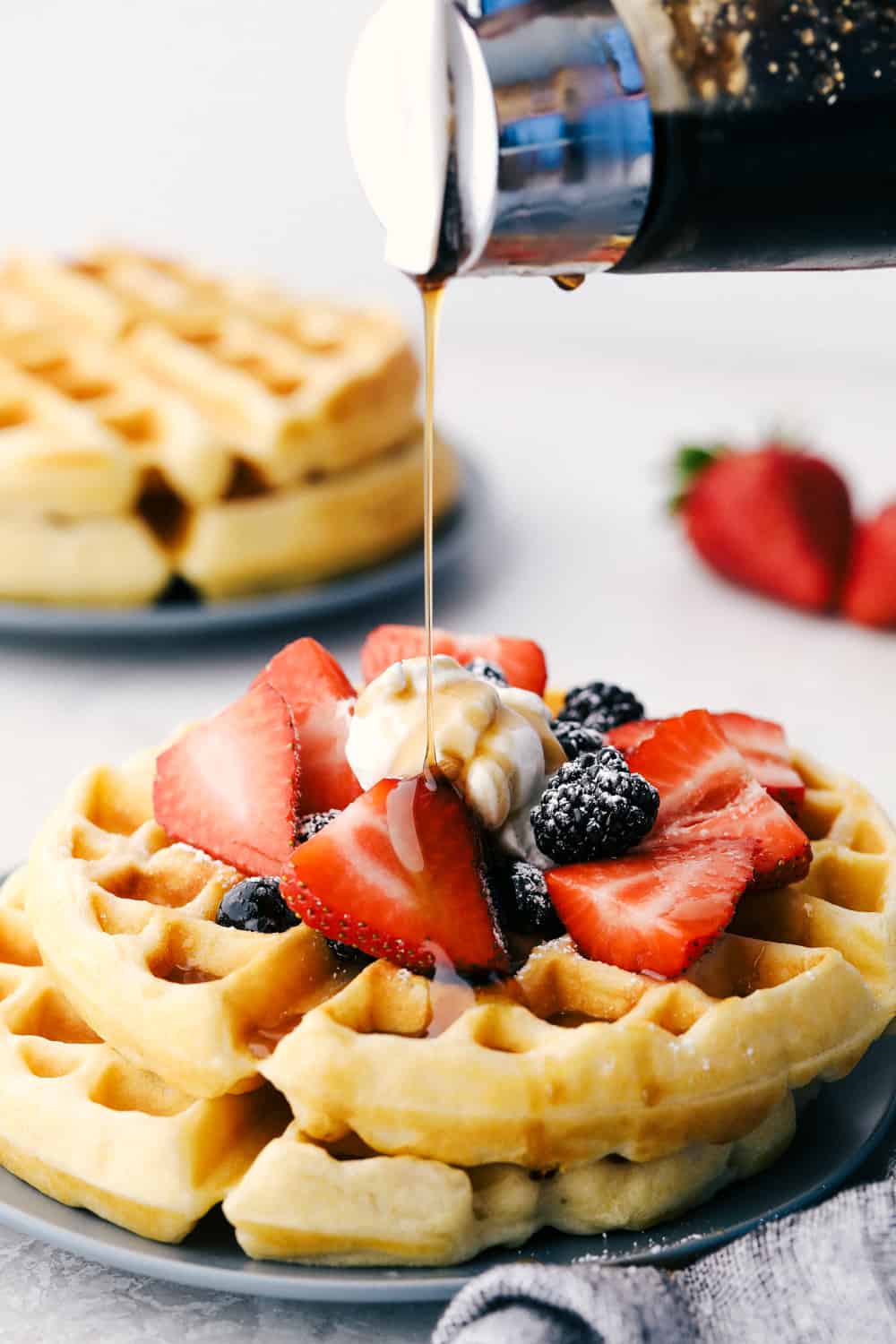 Pouring syrup over waffles with fruit and whipped cream. 