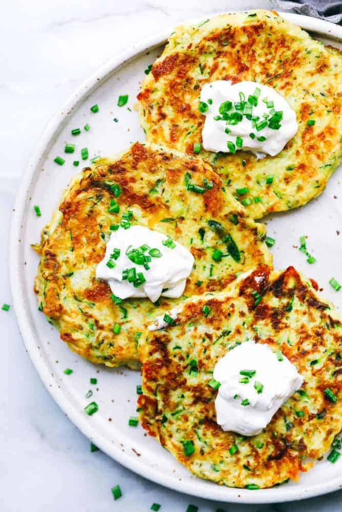 Three Cheesy Zucchini Fritters on a white plate. 