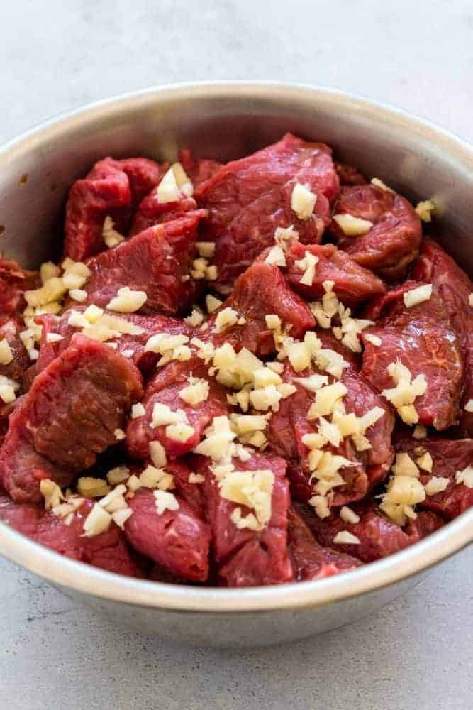 Beef chuck in a bowl with raw pieces of garlic and ginger.