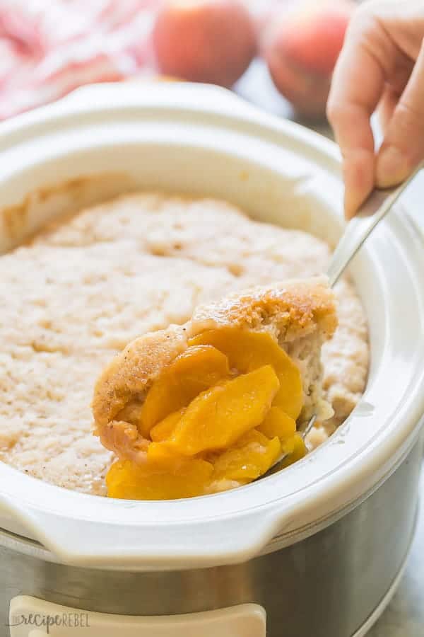 Peach cobbler in crock pot with a spoonful being removed. 