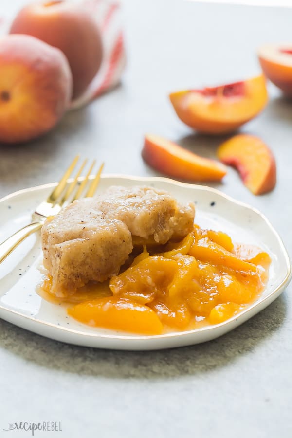 Peach cobbler on white plate with fresh peaches in the background. 