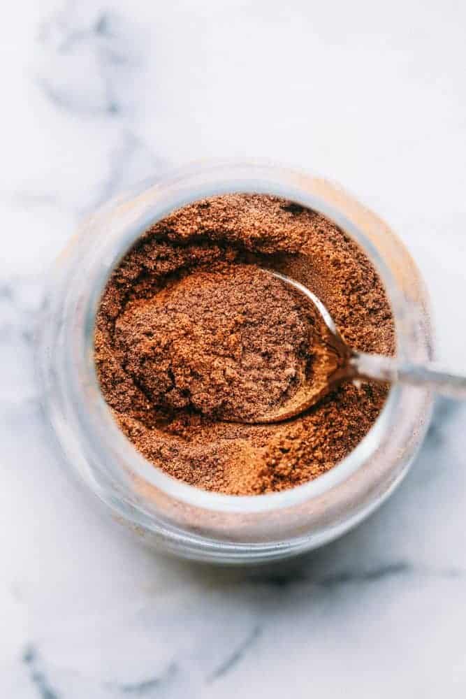 The top view of pumpkin pie spice in a clear glass jar with a metal spoon. 