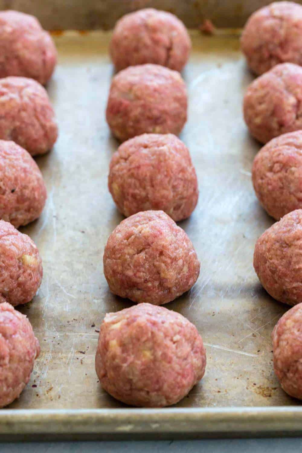 Raw meatballs lined up on a sheet pan