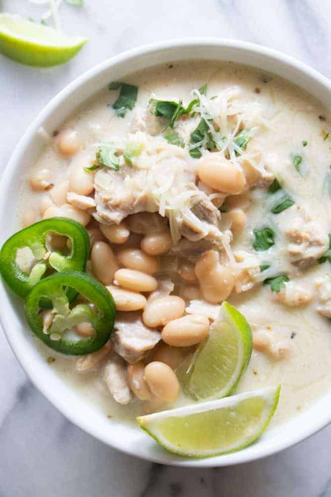 White bowl of Creamy White Chicken Chili with freshly sliced jalapeño and lime on top. 