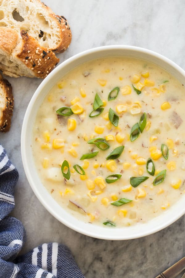 Corn chowder in a white bowl with fresh cut bread on the side.