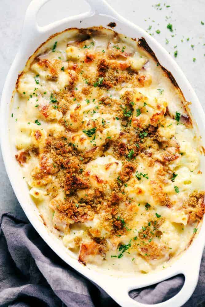 Creamy cauliflower gratin with bacon baked in a white casserole dish garnished with parsley.
