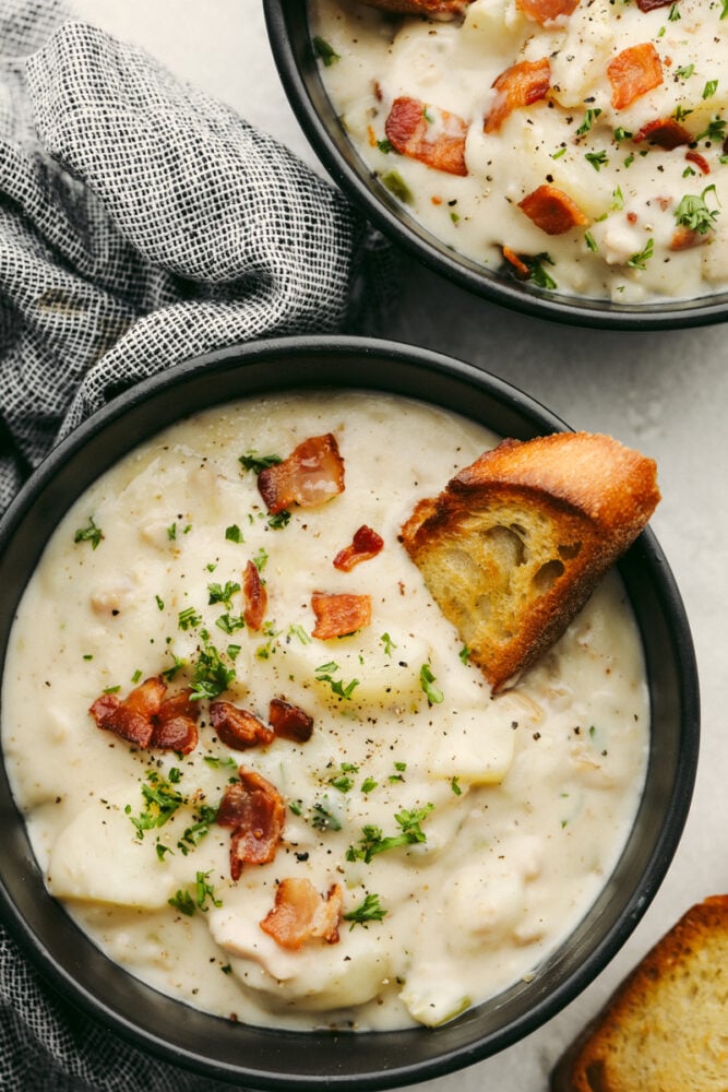 A bowl of clam chowder with a crostini in it. 