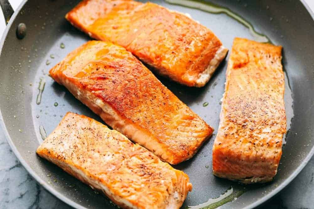 Salmon fillets being cooked in a frying pan getting ready for the creamy Tuscan garlic sauce. 