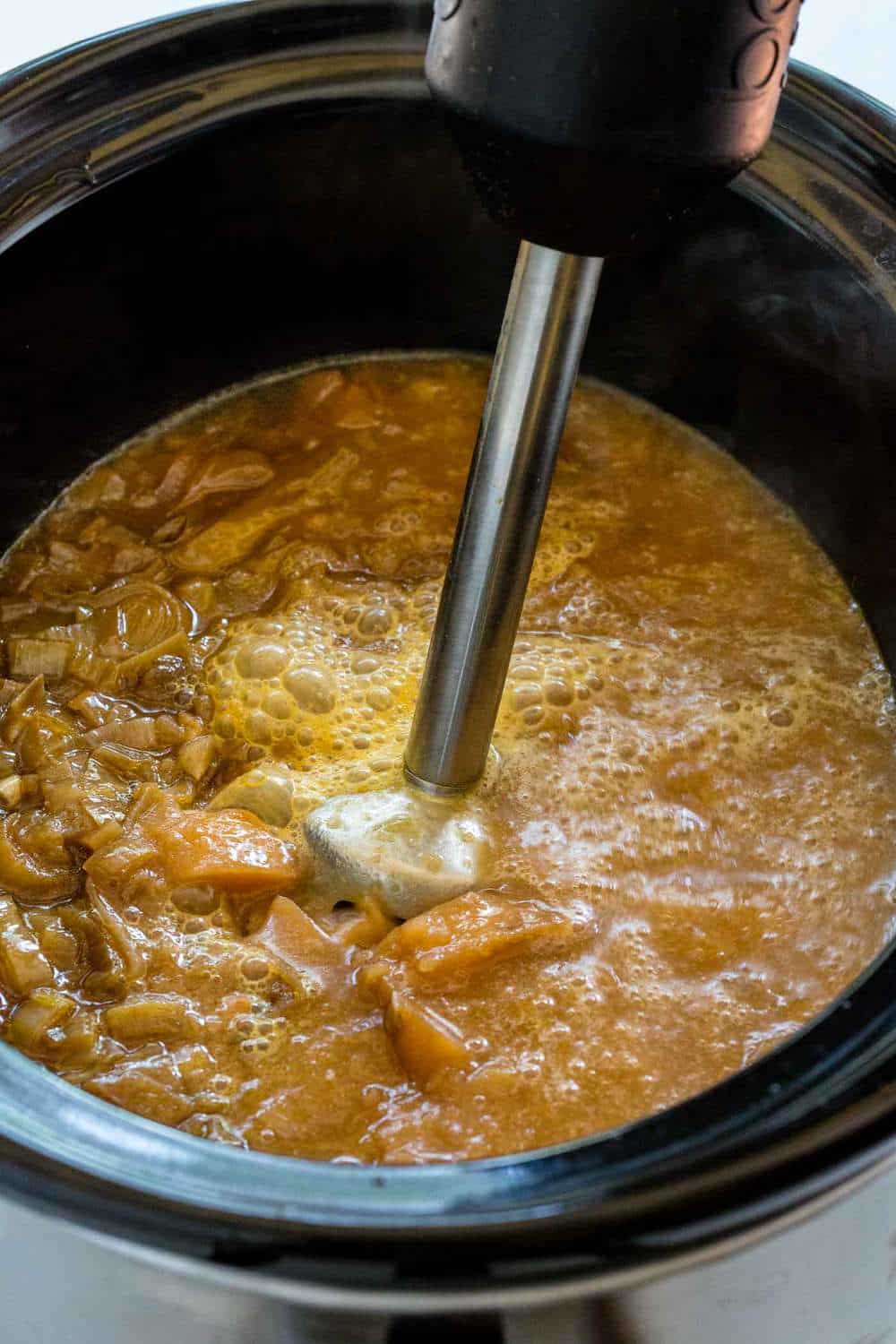 Immersion blender being used to mix the potato leek soup inside a Crock Pot