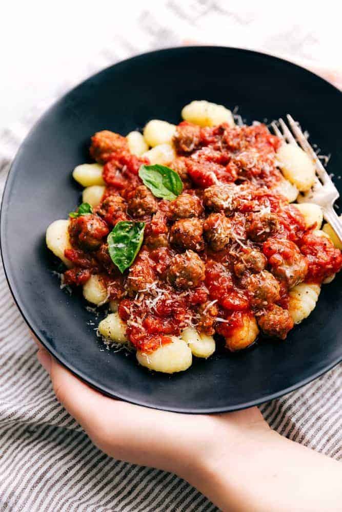Sausage tomato gnocchi in a black bowl with a fork on the side.