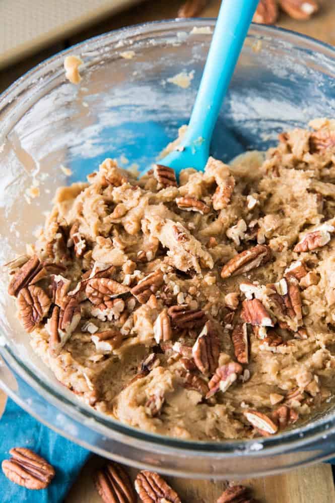 Butter pecan cookie mix in a glass bowl using a blue spoon stirring it together.