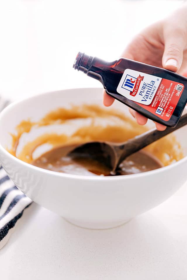 McCormick pure vanilla is being poured into a white bowl with the batter in it with a wooden spoon.
