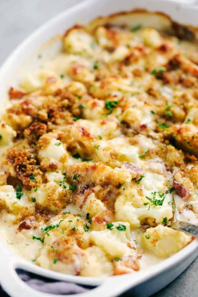 Creamy cauliflower au gratin with bacon and a white casserole dish garnished with parsley on top.