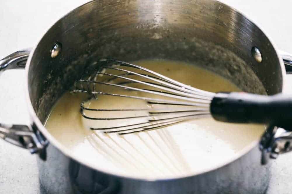 Au gratin in a sauce pan being boiled and stirred using a whisk.