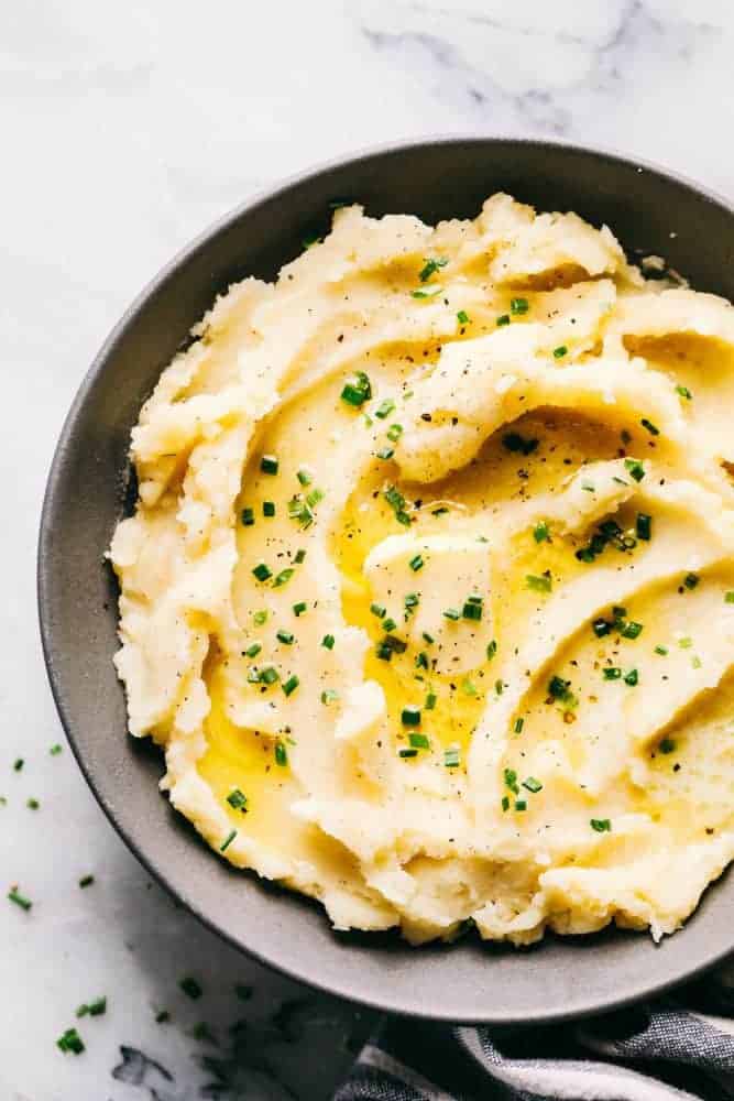Dad's famous mashed potatoes in a gray bowl topped with butter and chives.