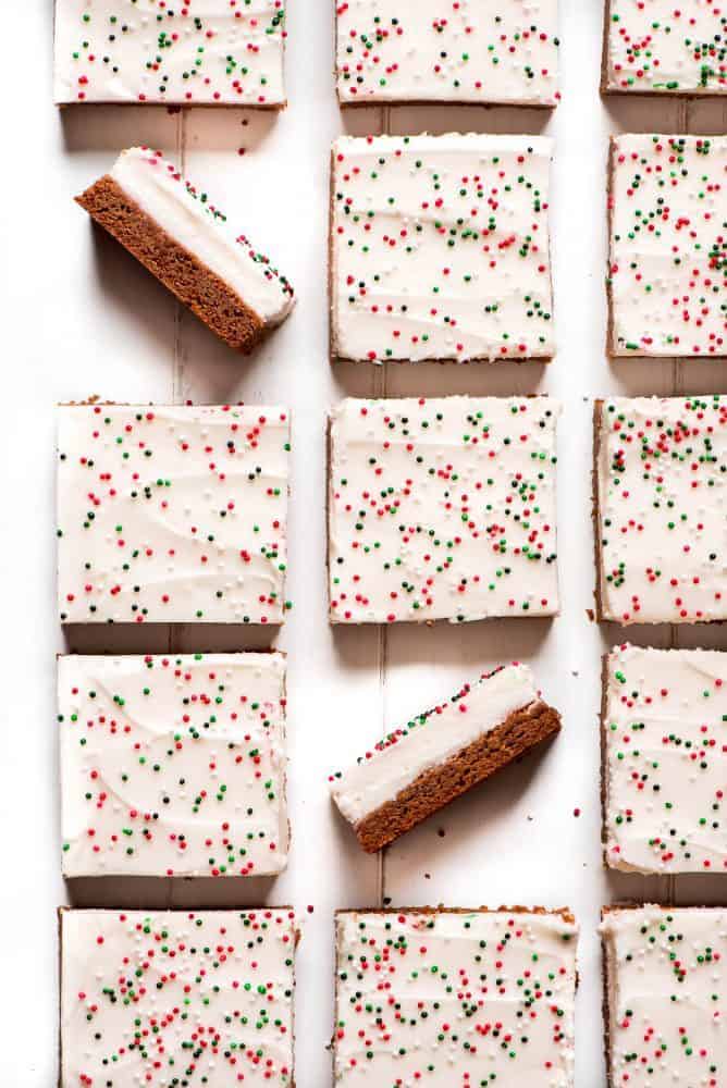 Gingerbread sugar cookie bars lined up cut into 2" x 2" pieces with two cookie bars facing upward to show the frosting and the cookie.