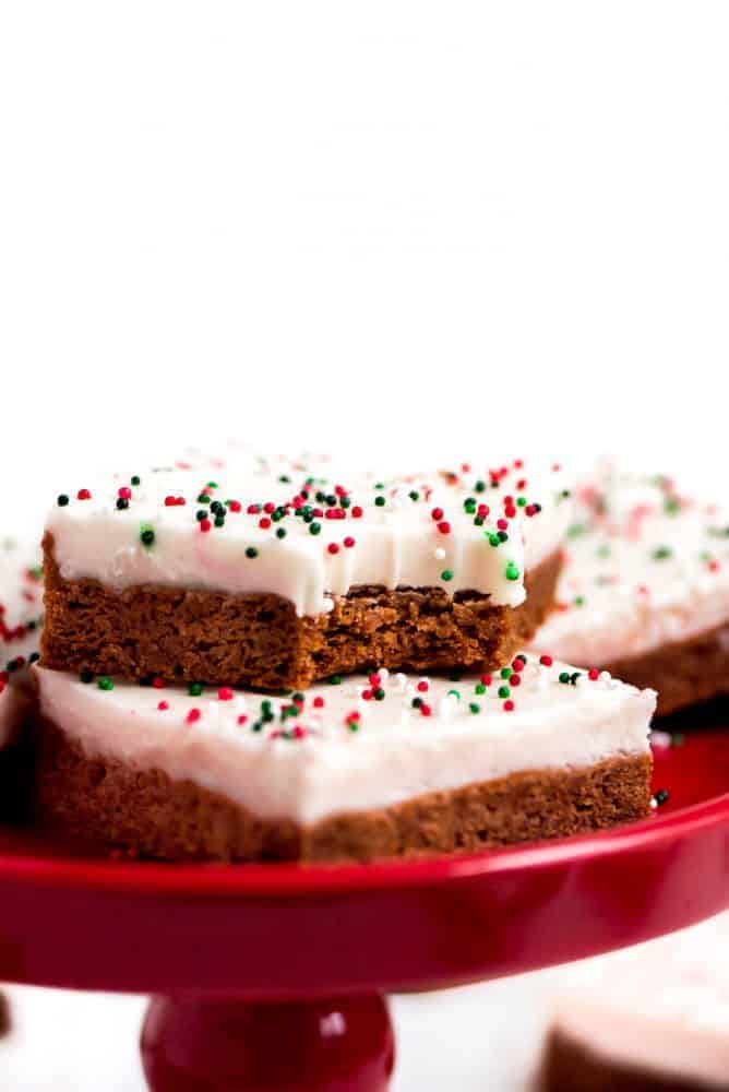 Gingerbread sugar cookie bars stacked on top each other with red and green sprinkles over top served on a red cake stand. 