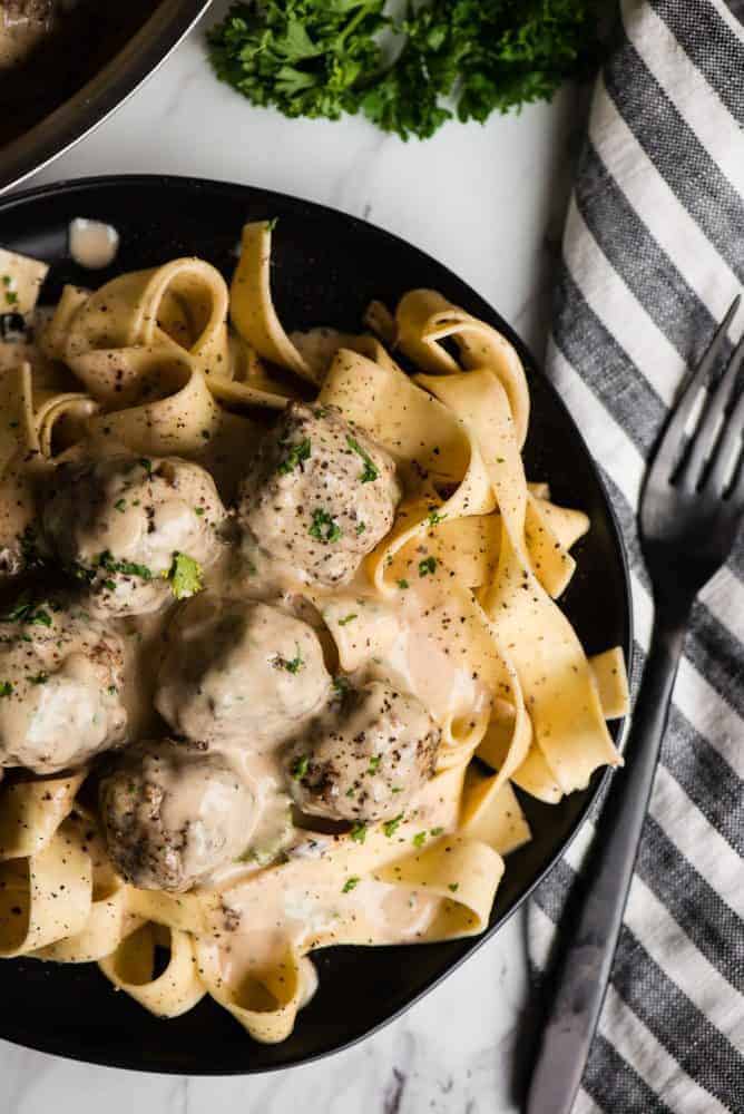 Swedish Meatball pasta on a black plate with a black fork on a napkin next to the plate on the righthand side.