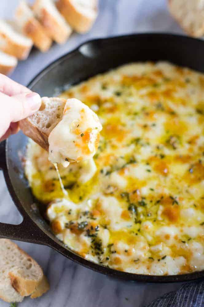 Baked Fontina Cheese Dip in a skillet with a hand dipping a piece bread. 
