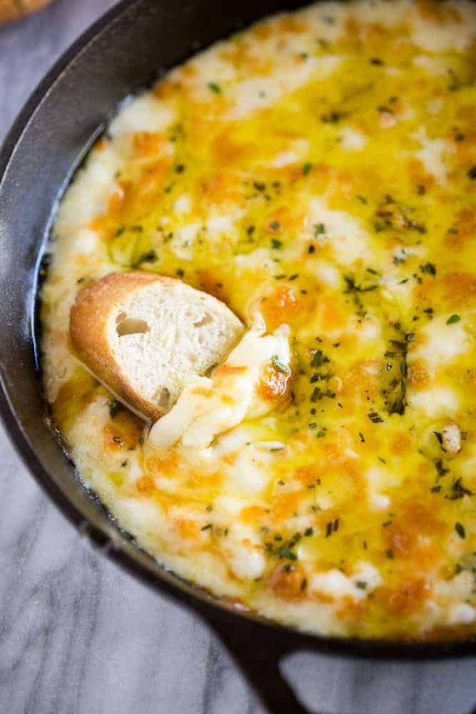 Baked fontina in a skillet with a piece of bread being dip in it.